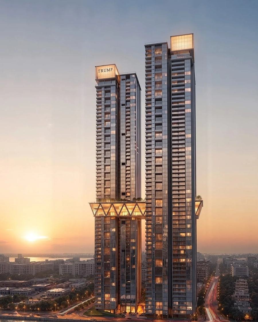 Trump Towers Kokapet at dusk: two 65-storey towers on Golden Mile Road, Hyderabad, with illuminated TRUMP crown signage and the suspended Trump Club sky bridge spanning both towers